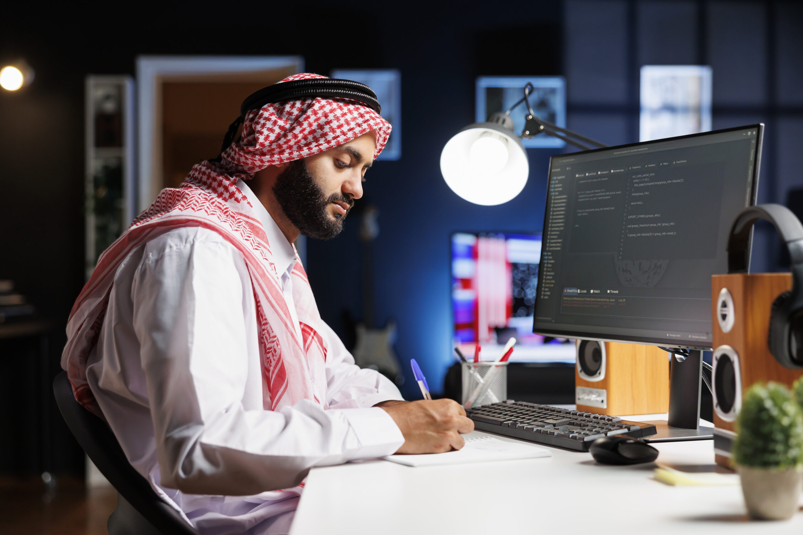 Man sits at a computer displaying codes Muslim man sits at a computer and programs, exhibiting the app development process. Side-view image of a computer monitor displaying algorithms created by an Arab guy dressed traditionally.